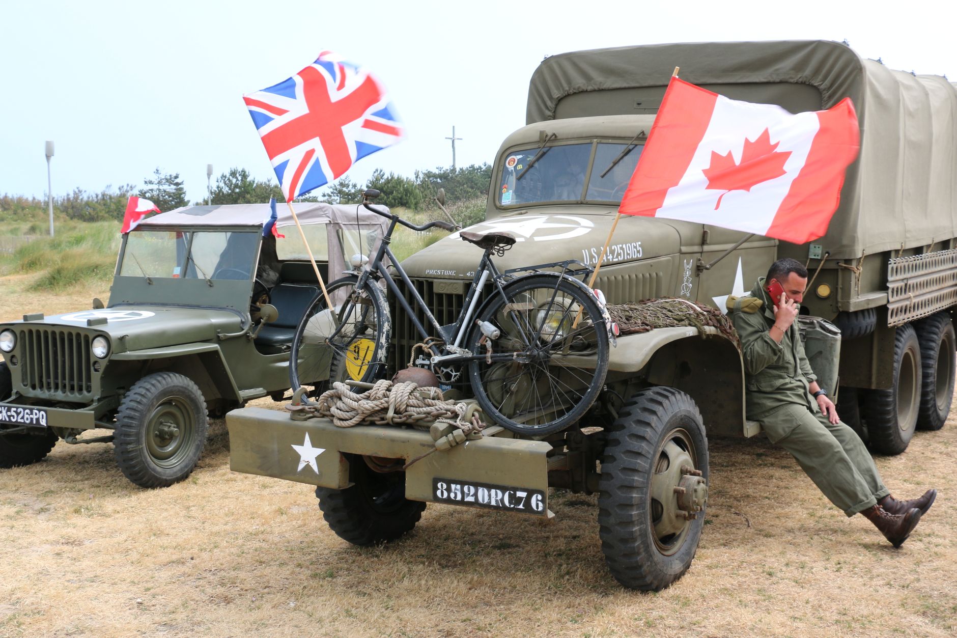 Scene of vintage military vehicles with British and Canadian flags and a bicycle.