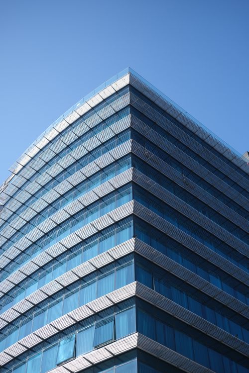Free A low angle shot of a modern office building with sleek glass windows against a blue sky. Stock Photo