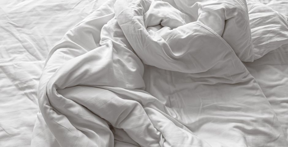 Crumpled white hotel bedding — bed bugs hide in mattress seams and headboards