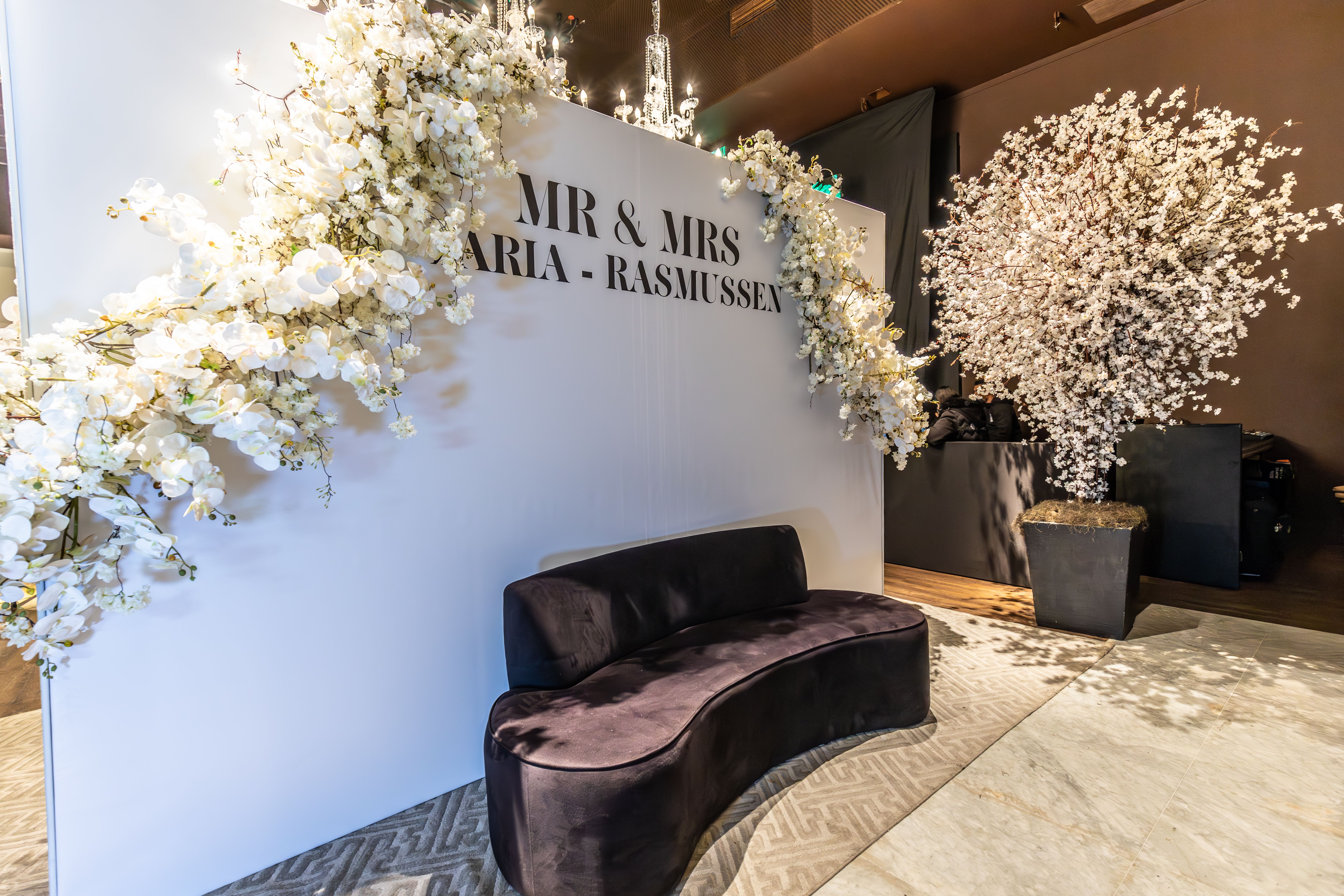Stylish wedding reception setup with white floral decor, sofa, and elegant backdrop.