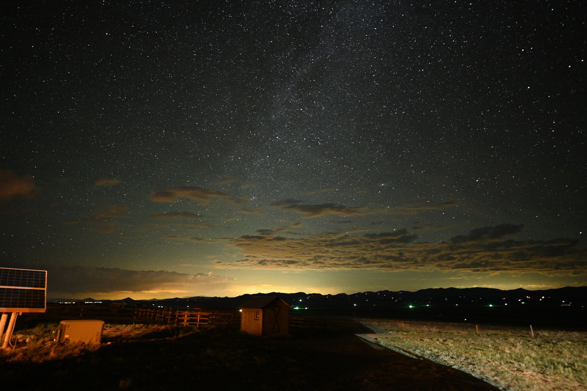 A breathtaking view of a star-filled night sky over a rural landscape, with visible clouds and distant lights.