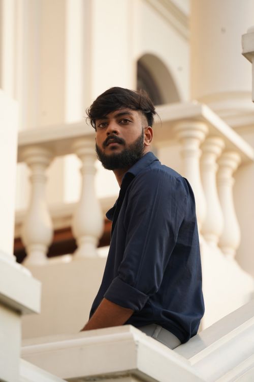 Free Portrait of a young man with a beard, sitting and posing on a staircase indoors. Stock Photo