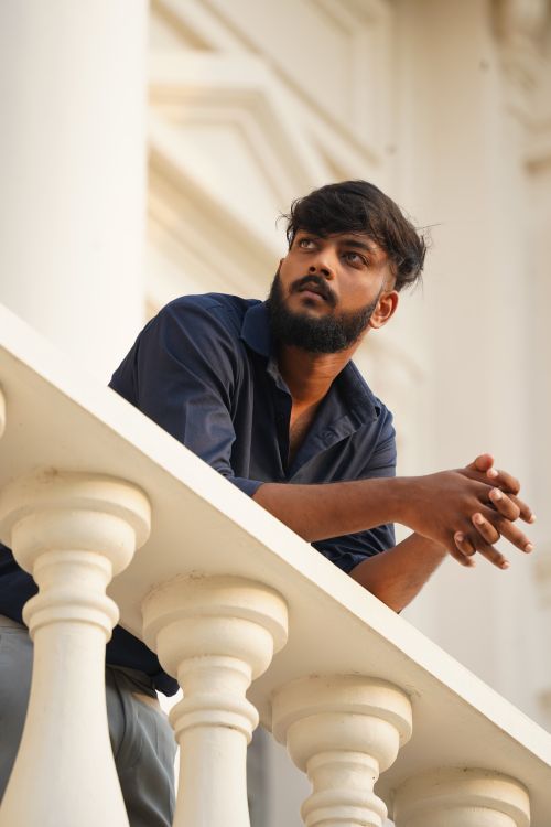 Free Portrait of a thoughtful man leaning on an ornate balcony in a city setting. Stock Photo