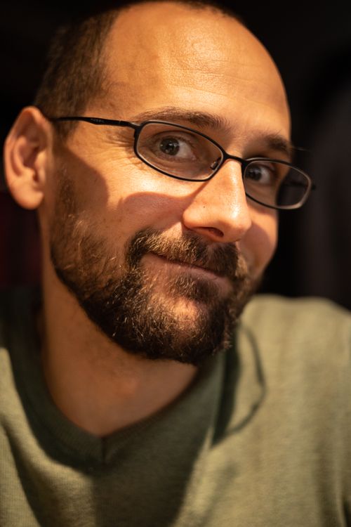Free Close-up portrait of a smiling man wearing glasses and a beard in a warm, indoor setting. Stock Photo