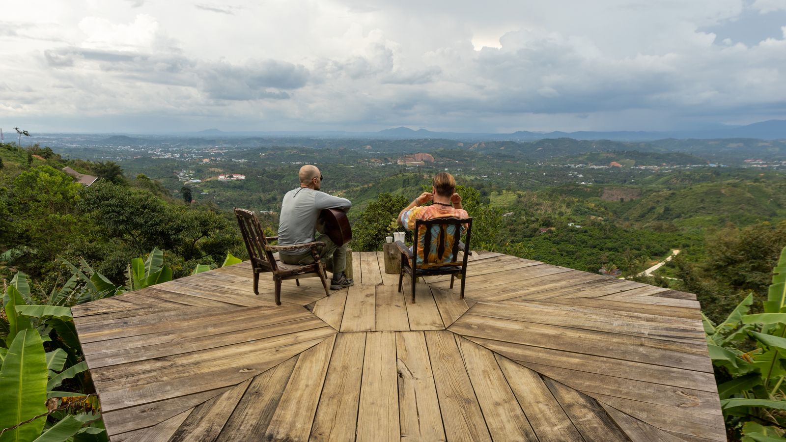 Men sitting on terrace over forest and playing music, DR Congo