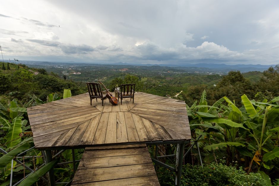 Elevated wooden deck overlooking lush greenery and mountains with two chairs and a double bass.