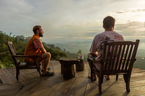 Free Two men enjoy a peaceful sunrise view from a mountain deck, perfect for a tranquil getaway. Stock Photo