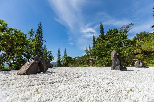Free Peaceful Zen garden with stone sculptures set against a vibrant green backdrop and clear blue sky. Stock Photo