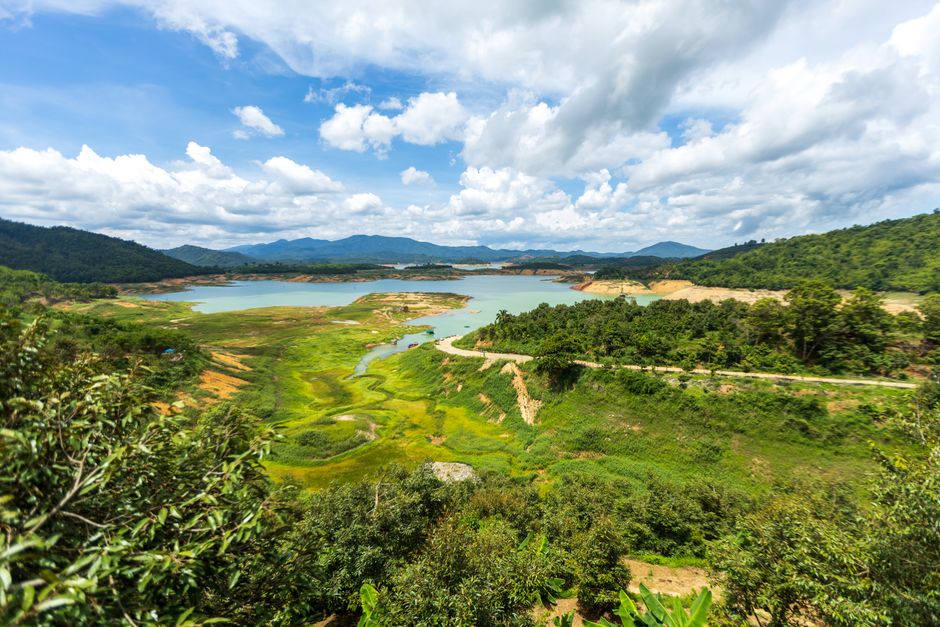 A breathtaking aerial view of a vibrant landscape featuring green hills and a tranquil lake under a bright blue sky.