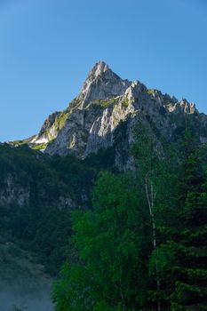 Capture the stunning beauty of a mountain peak in Podgorica, Montenegro, surrounded by lush greenery.