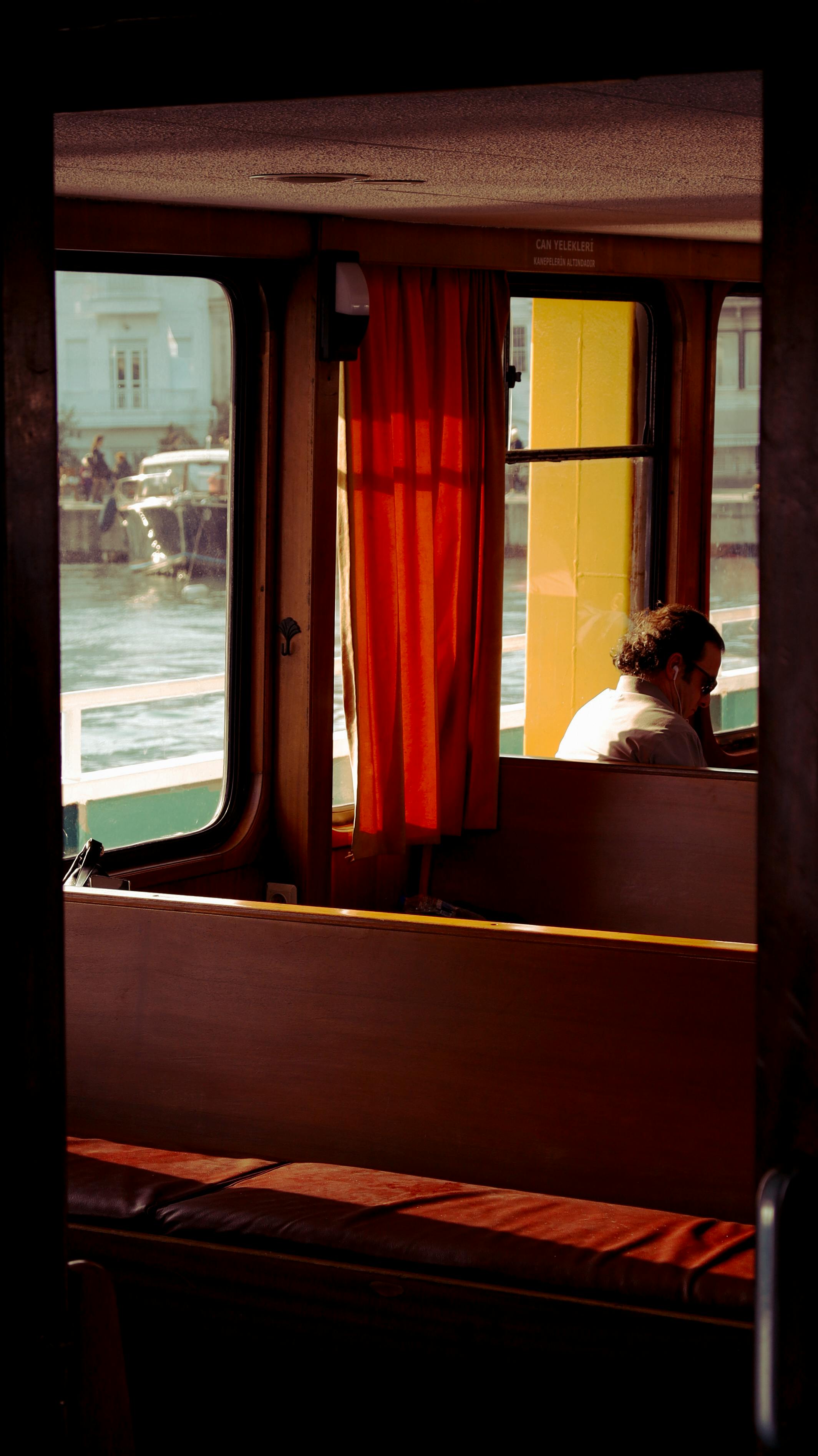 A peaceful moment inside a ferry with a man gazing out the window, capturing sunlight and reflections.