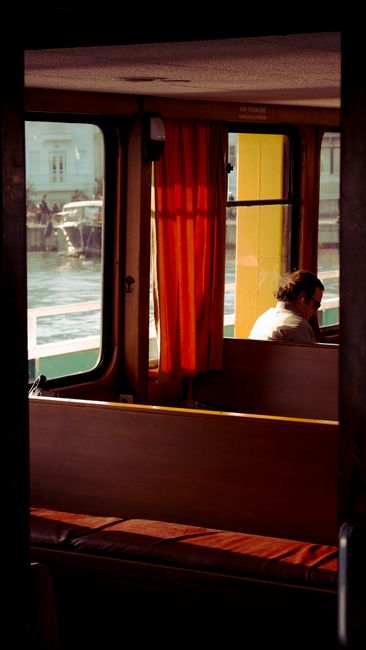 A peaceful moment inside a ferry with a man gazing out the window, capturing sunlight and reflections.