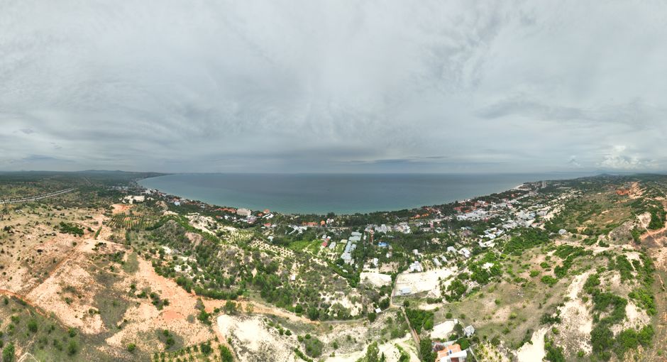 Expansive aerial view of a coastal town overlooking the sea under an overcast sky, showcasing natural landscapes and urban areas.