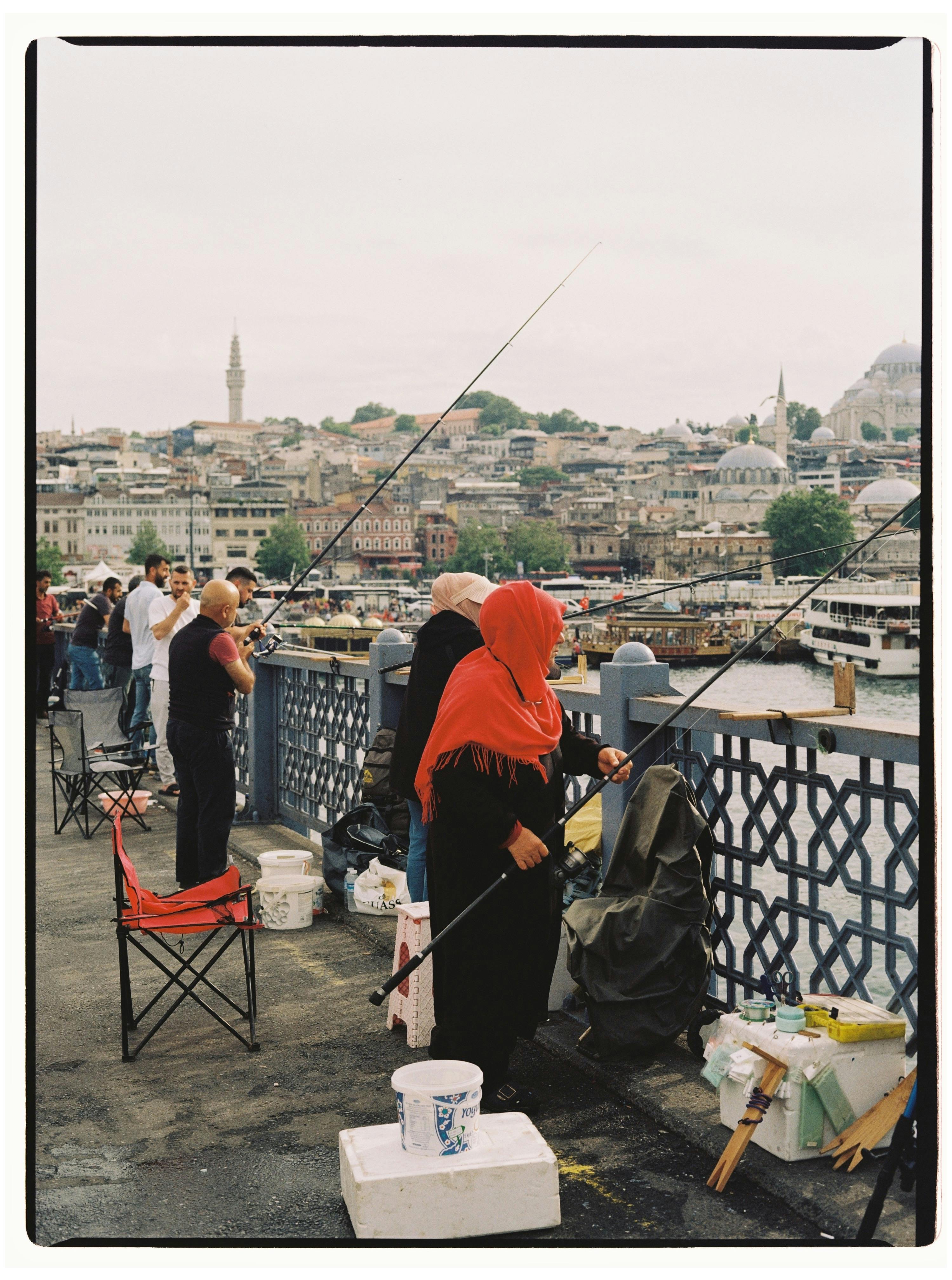 Fishermen casting lines on Galata Bridge with Istanbul cityscape in the background.