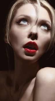 Close-up portrait of a woman with an expressive, surprised look and bold red lips on a dark background.