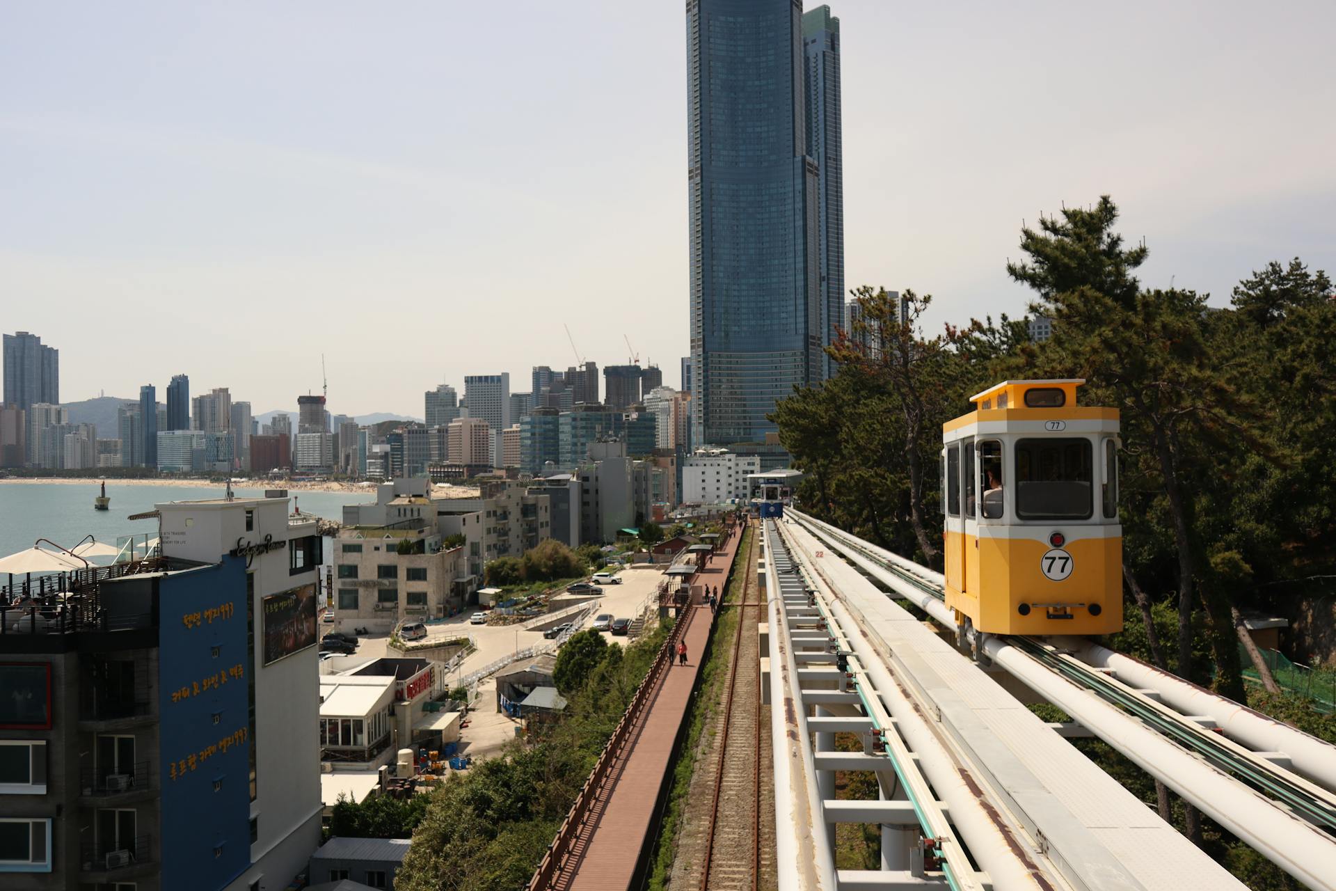 Vibrant urban scene in Busan featuring elevated train with skyscrapers and coastal view.