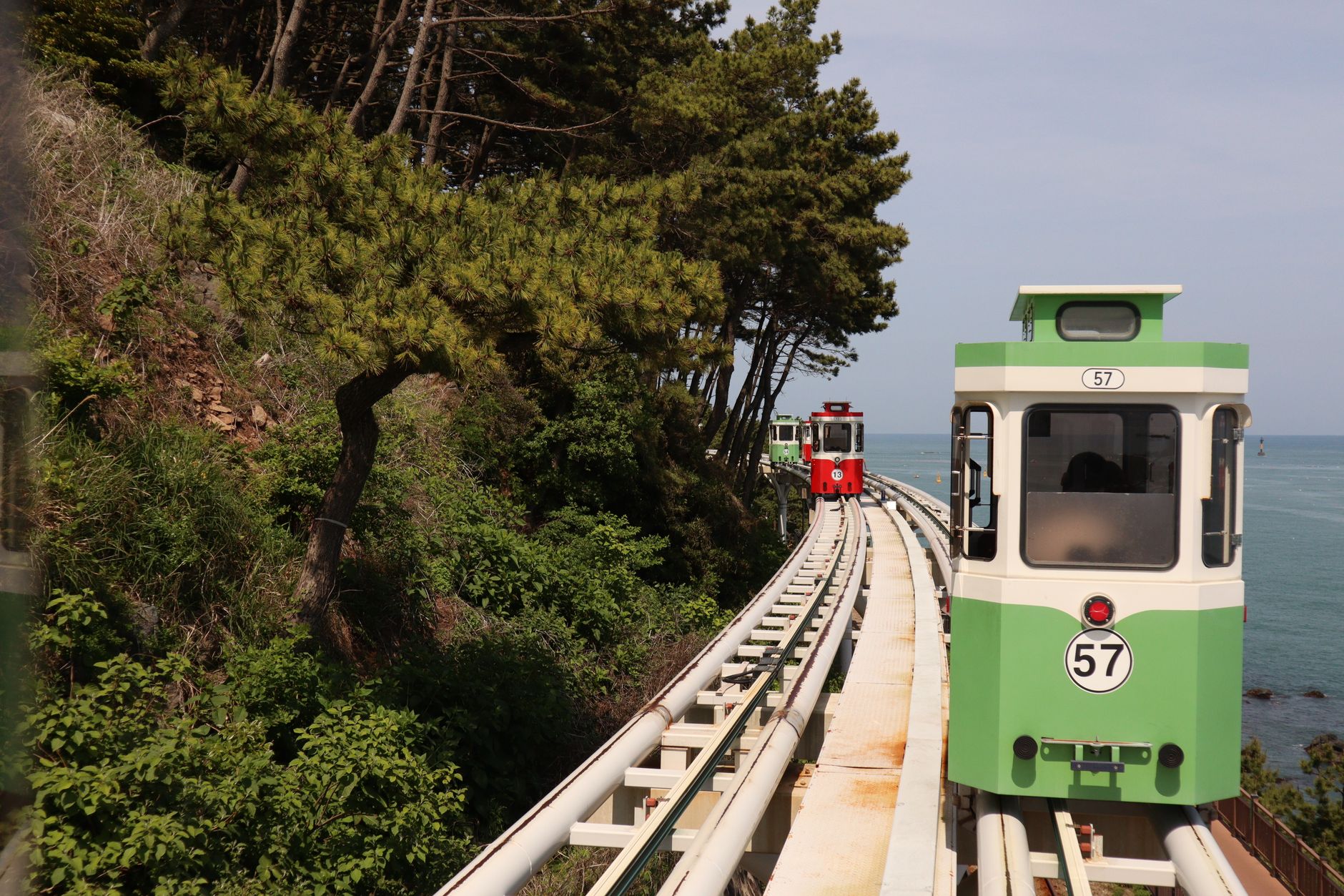 The green and red Sky Capsules of Haeundae Blueline Park running along the elevated coastal track above the sea