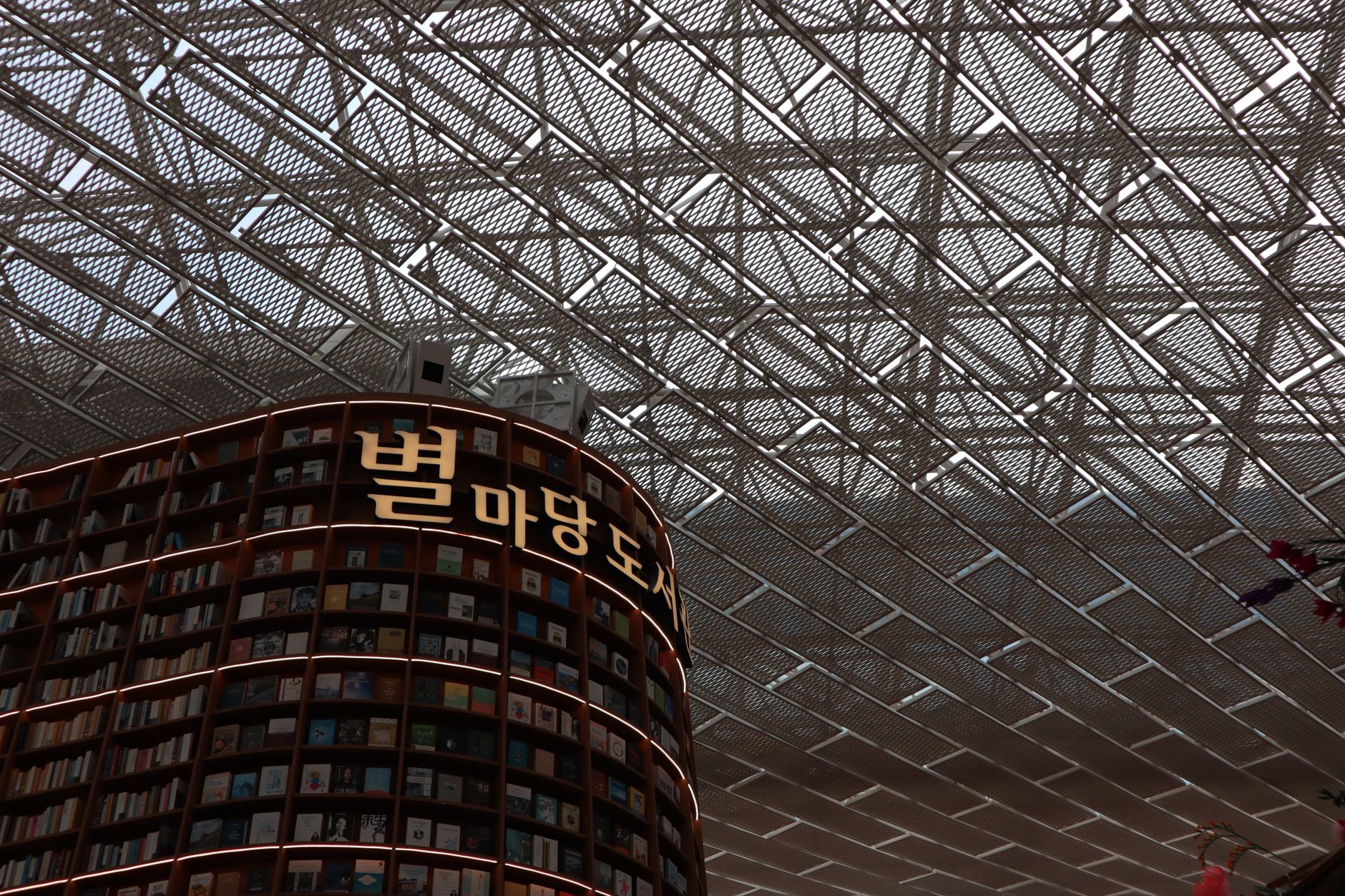 A modern library interior featuring tall bookshelves and a geometric ceiling.