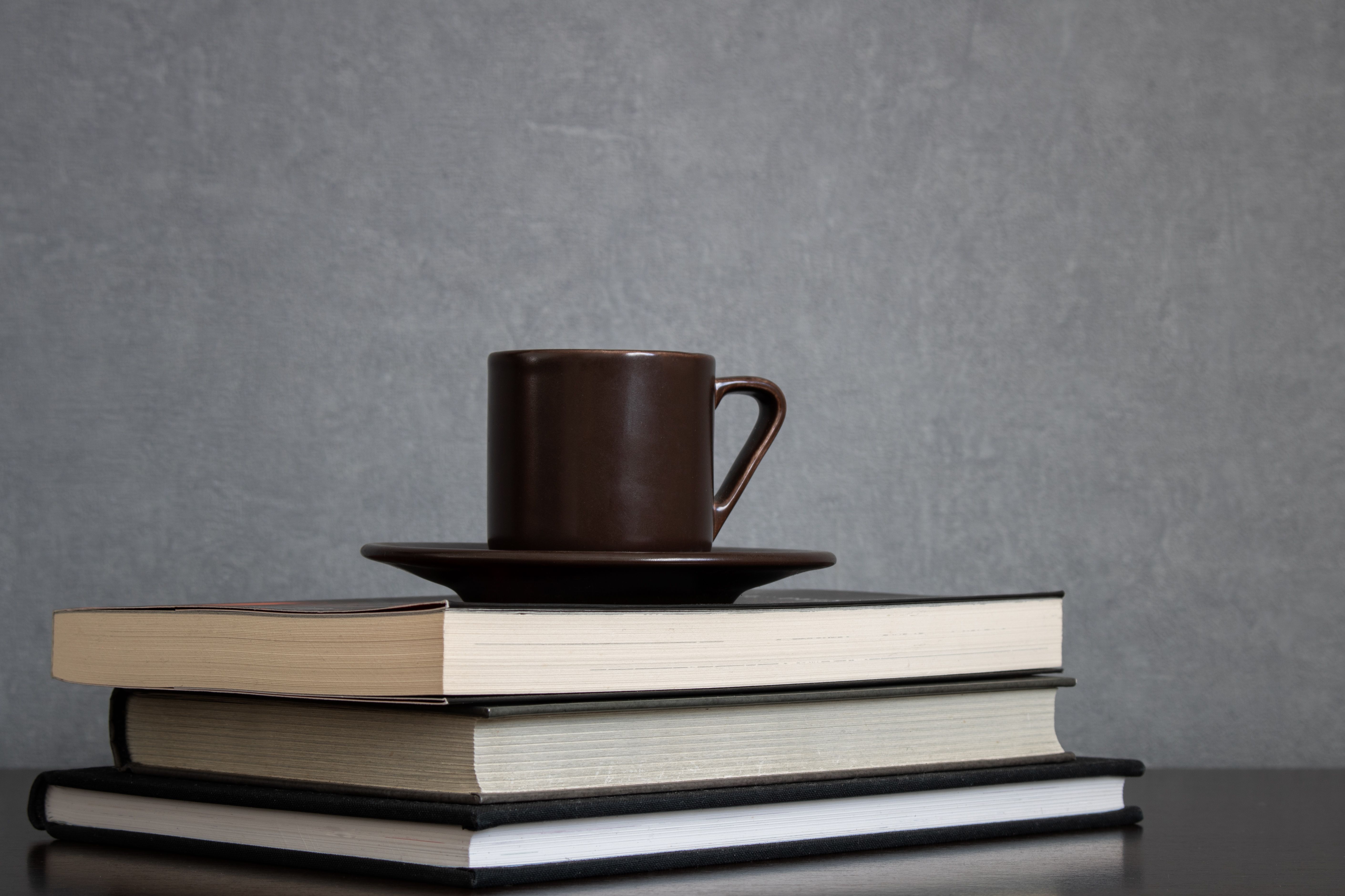 brown-cup-of-coffee-with-saucer-on-top-of-pile-of-books-to-read-placed