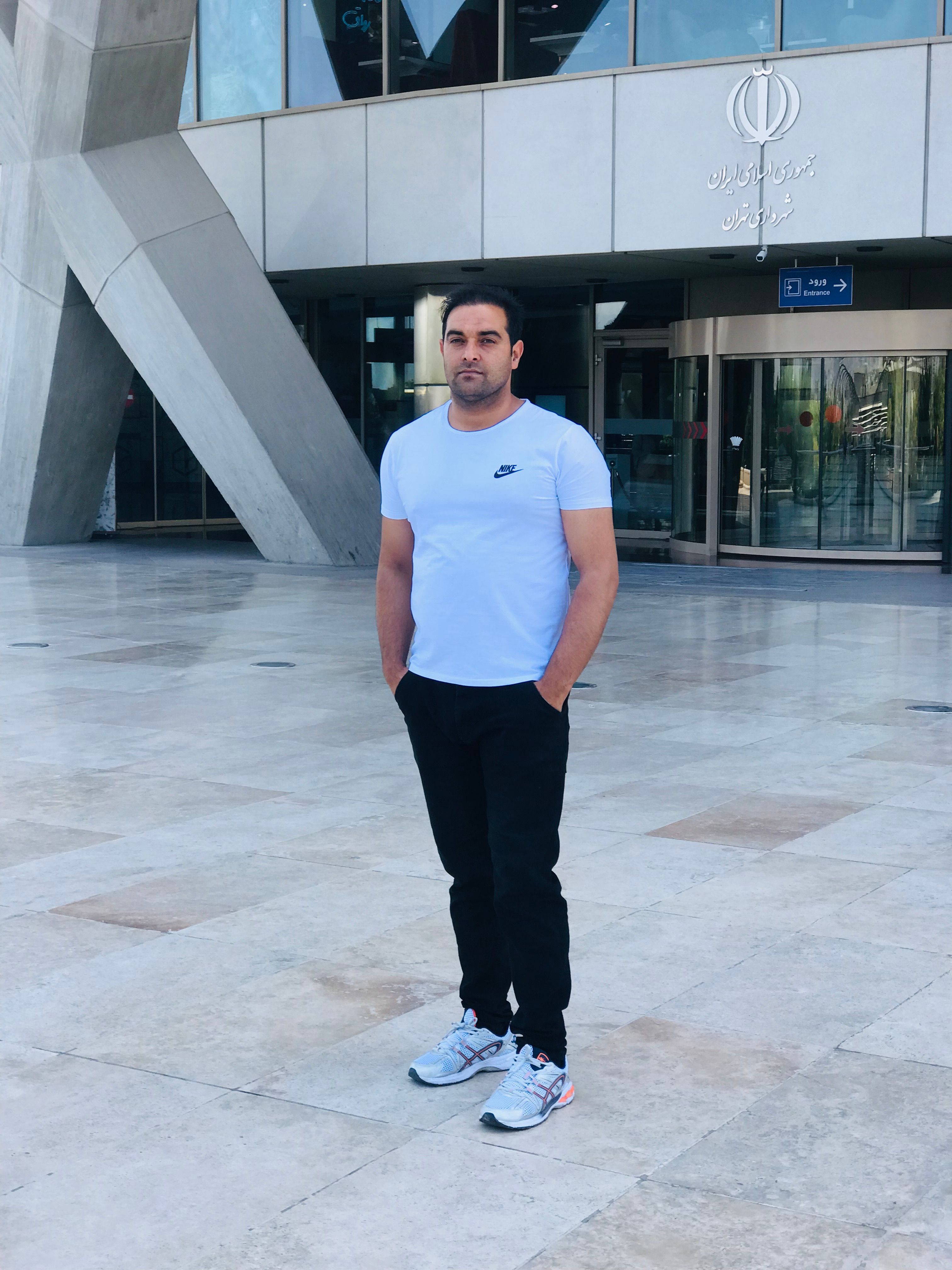 A man in casual attire stands in front of a modern building entrance during the day.