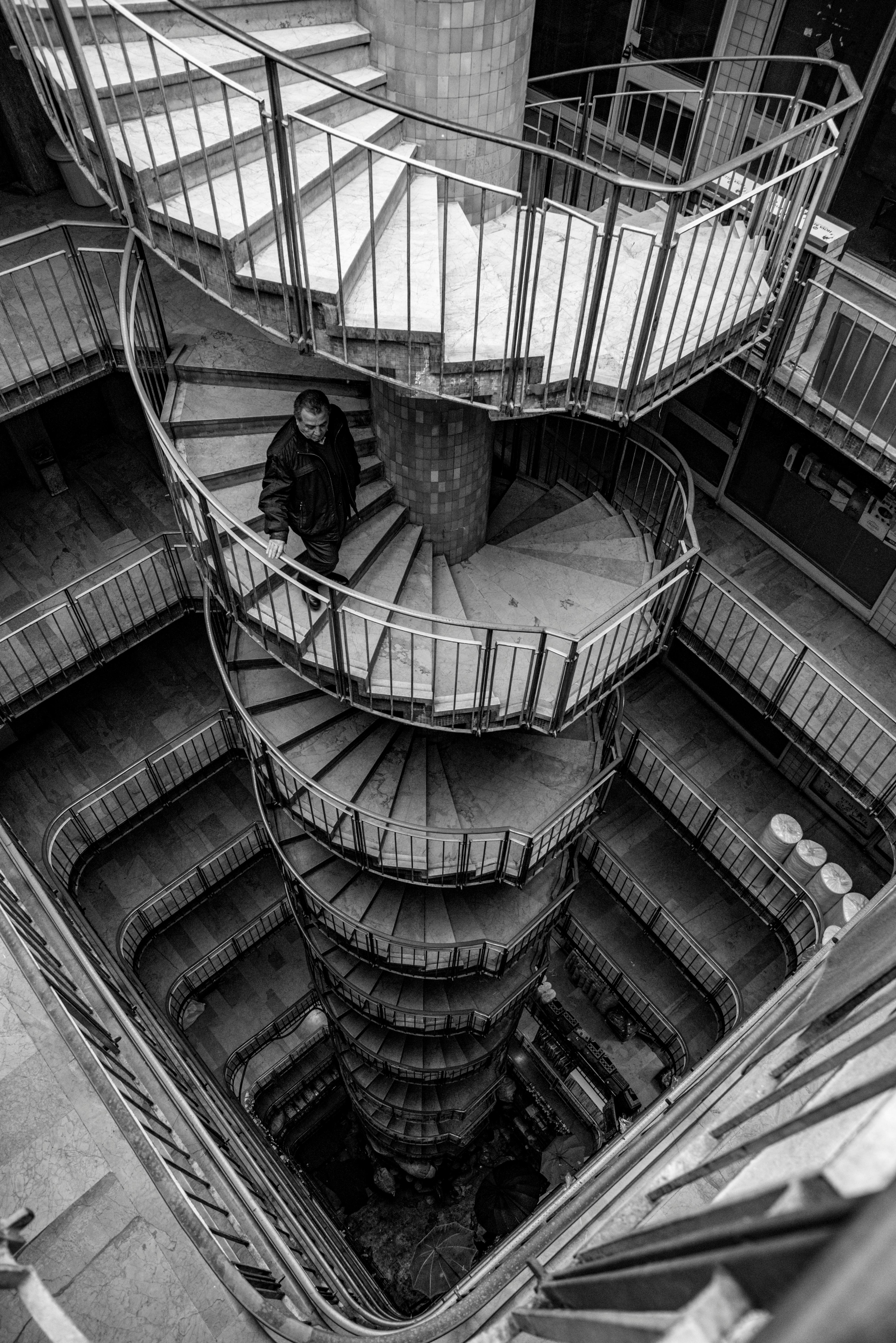 A man ascending a dramatic spiral staircase, captured in black and white.