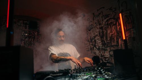 Free A DJ engrossed in music mixing in a foggy, ambient setting. Stock Photo