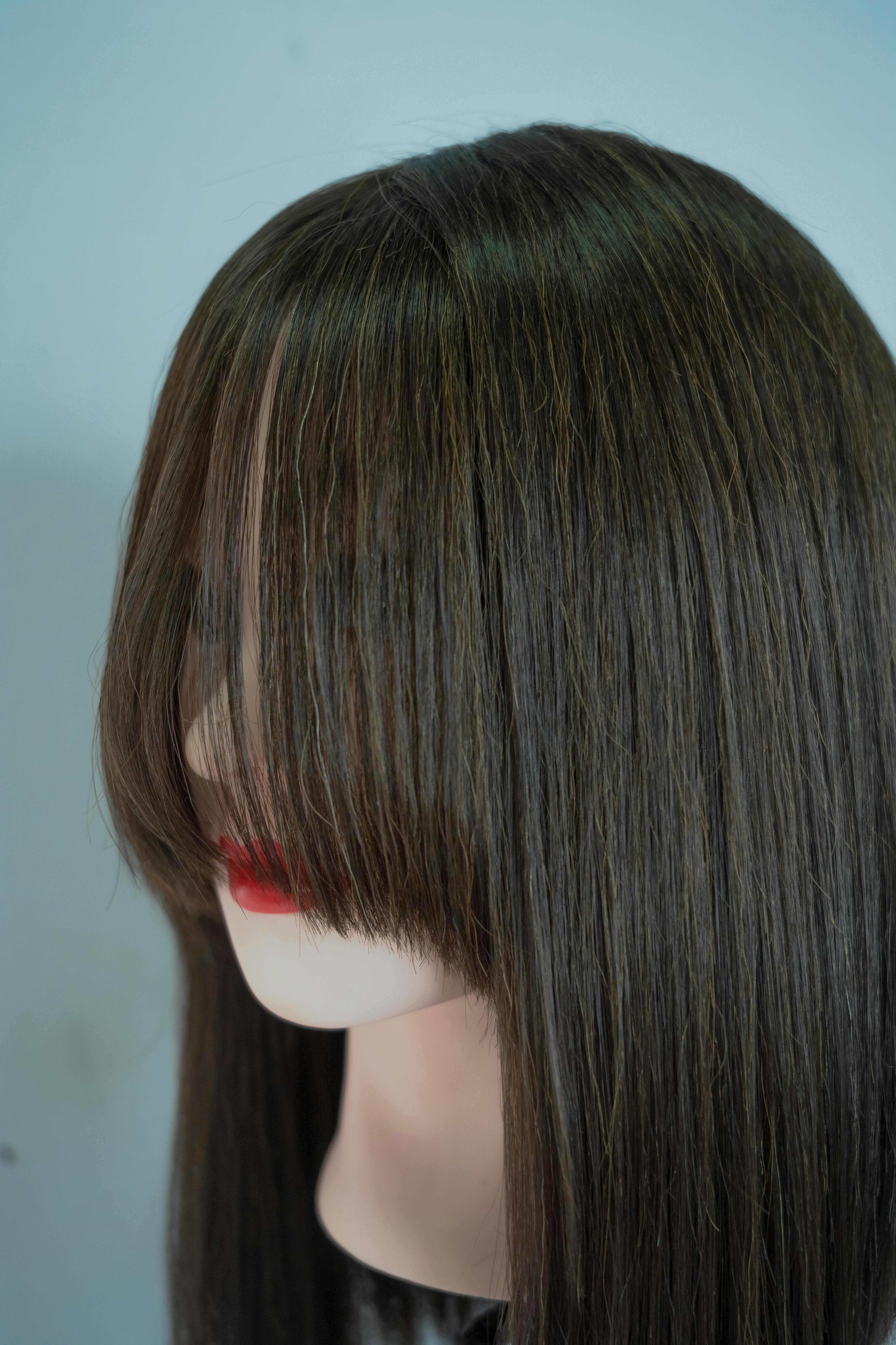 Close-up of a mannequin with long brown hair and red lips on a neutral background.