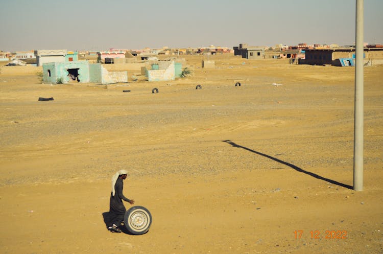 Man Rolling Wheel In Village On Desert