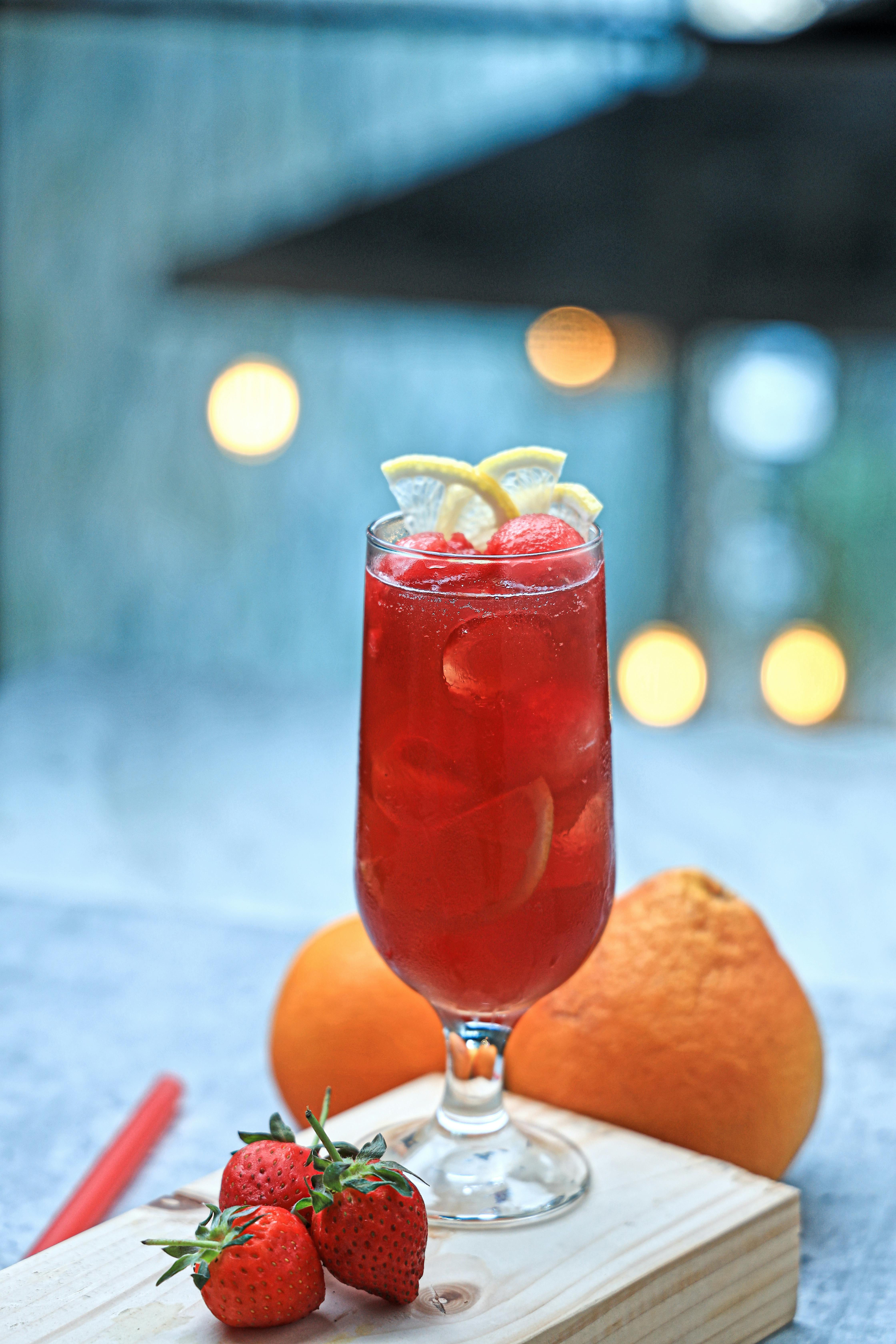 a glass of red drink with strawberries and oranges