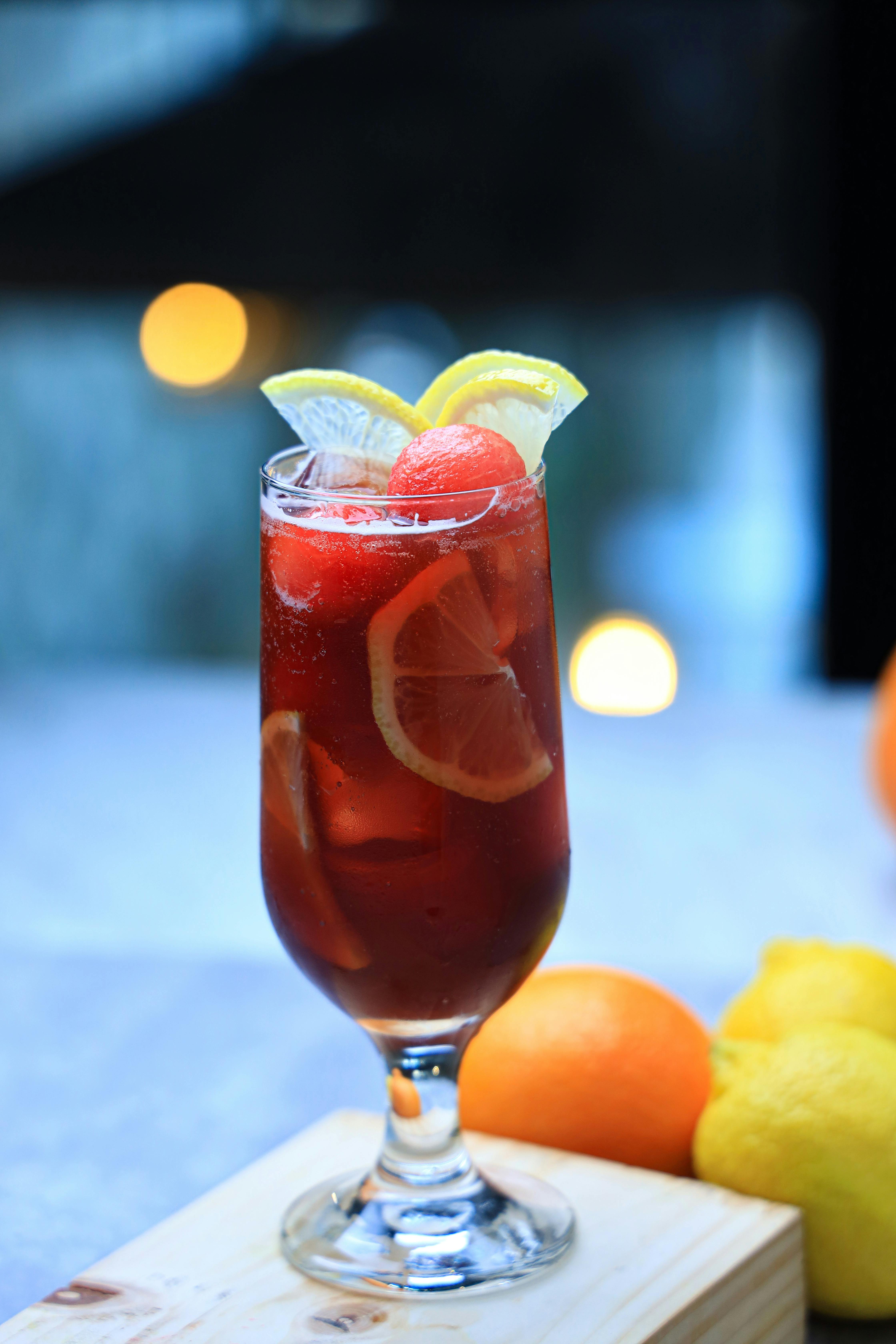 a glass of red drink with lemon slices and oranges