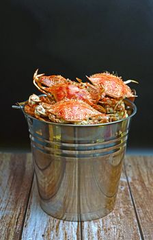 Close-up of freshly steamed crabs in a metallic bucket on rustic wood surface.