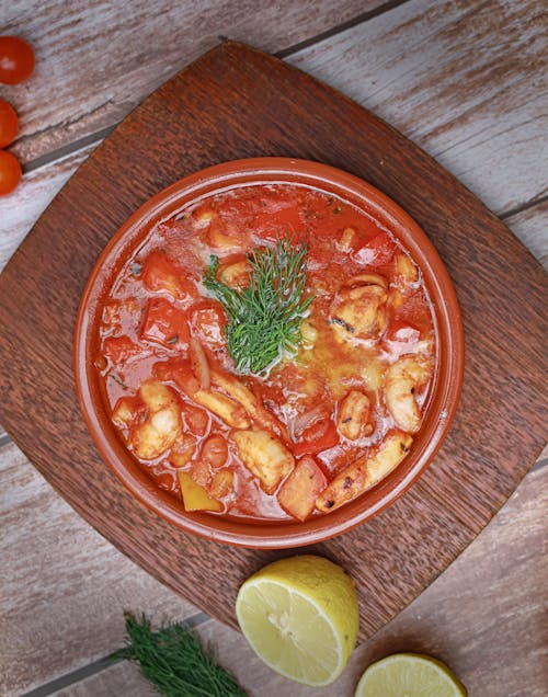 A bowl of stew with tomatoes, lemons and herbs