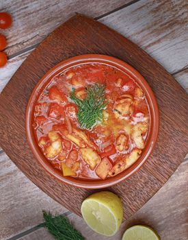 Savory seafood stew with tomato base served in a clay bowl, garnished with herbs, perfect for dinner.