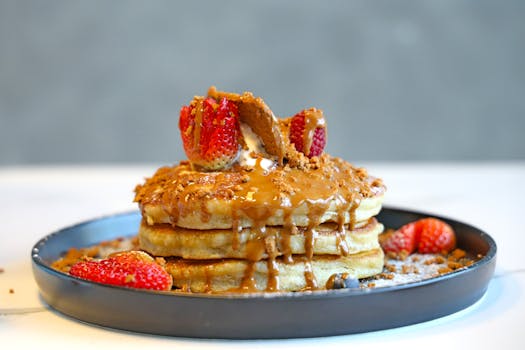 Mouth-watering stack of pancakes topped with strawberries and syrup, perfect for breakfast lovers.