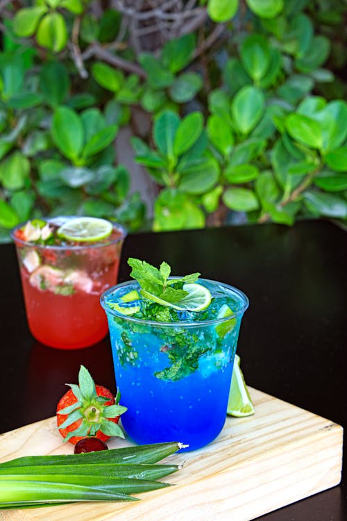 Two glasses of blue and green drinks on a cutting board