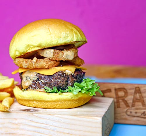 A burger with fries and onion on a wooden board