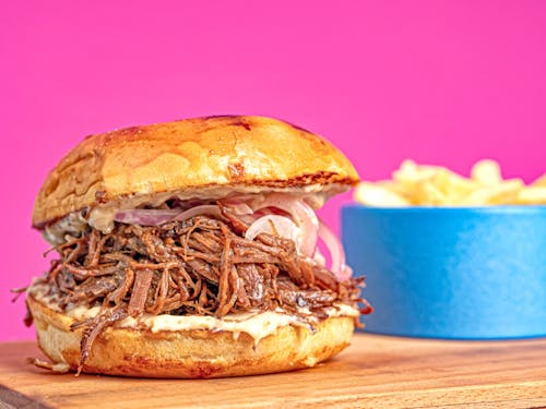 A pulled pork sandwich with chips on a wooden cutting board