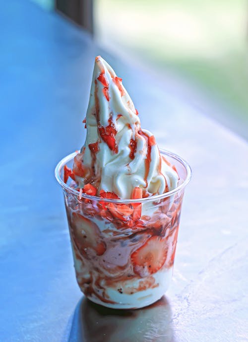 A small cup of ice cream with strawberries and whipped cream