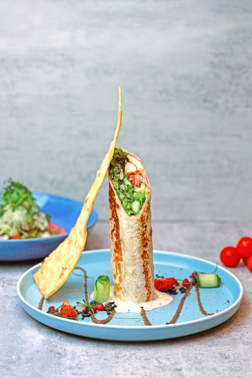 Free Delicious vegan wrap filled with fresh veggies and hummus, garnished with cucumber and tomatoes. Stock Photo