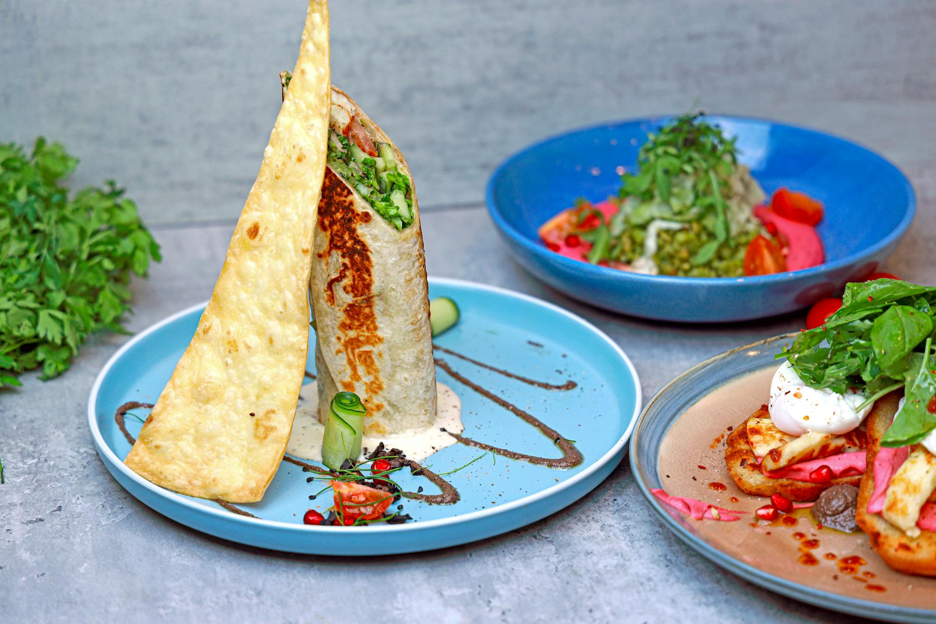 A vibrant display of gourmet brunch dishes on colorful plates, featuring wraps and fresh greens.