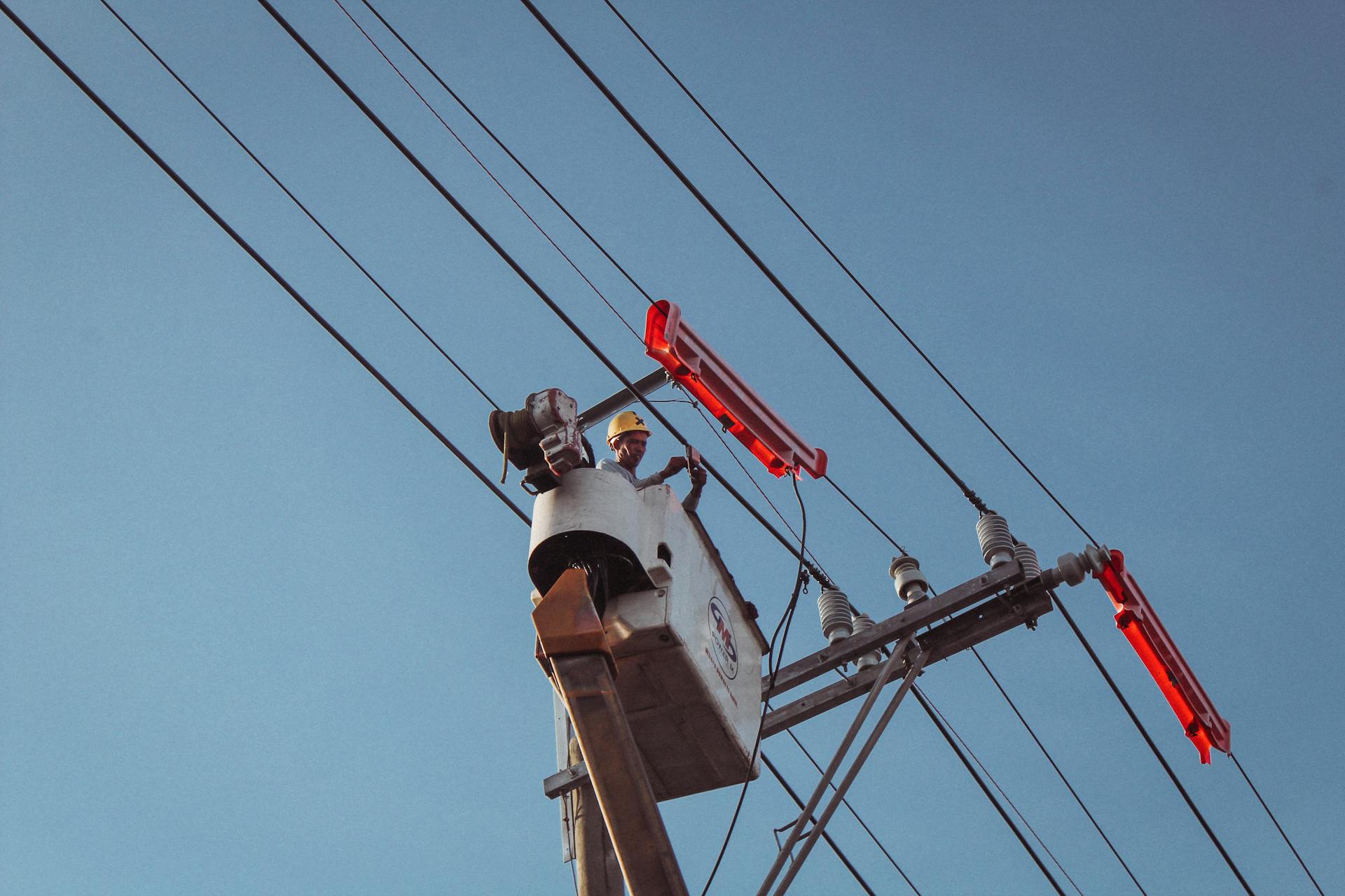 Electrician in a lift repairing overhead power lines on a clear day.