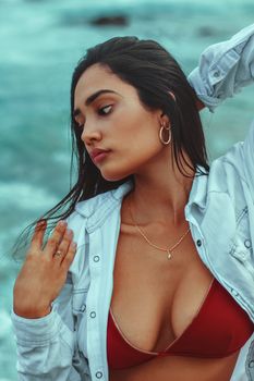 Stylish woman in red bikini and jacket posing by the ocean, showcasing natural beauty and elegance.