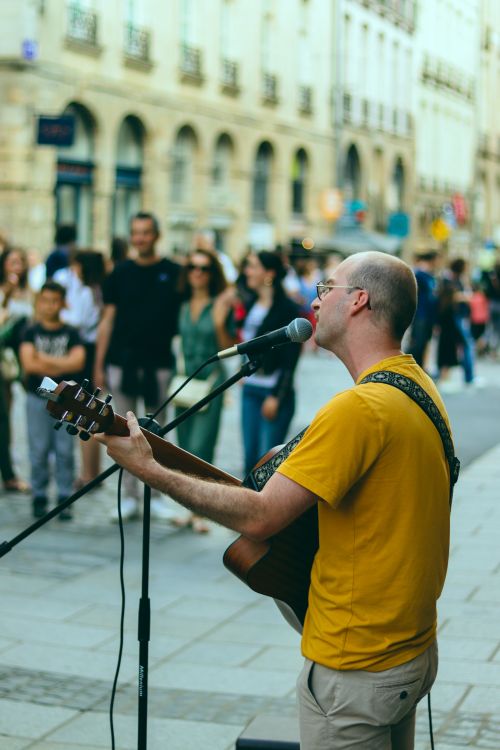 Free A street musician performing with a guitar and microphone on a busy street in Rennes, France. Stock Photo