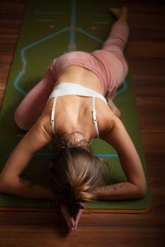 A woman doing yoga on a green mat with focus on stretching and relaxation.