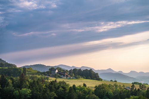 Free Peaceful aerial view of a house surrounded by lush greenery and rolling hills under a dramatic sky. Stock Photo