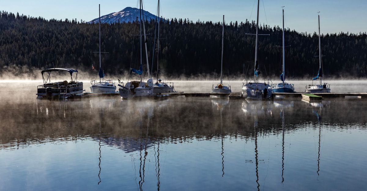 Calm morning at Elk Lake, Oregon with sailboats and mist over the water.
