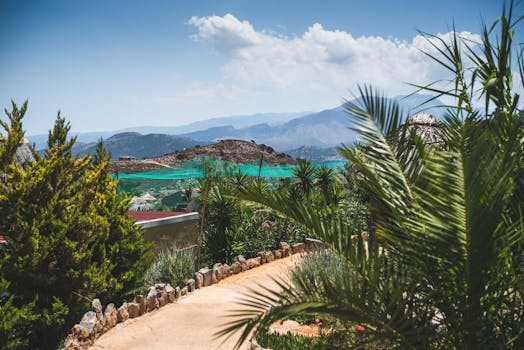 A picturesque pathway surrounded by lush greenery with mountains and blue sky in Rethymno, Greece.