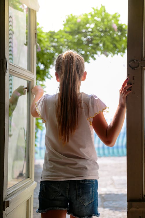 Back View of a Girl in a T-shirt and Shorts Standing in a Doorway 