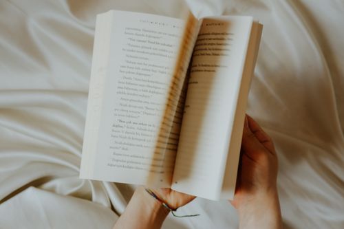 Free Hands holding an open book on soft fabric, captured in warm light. Stock Photo
