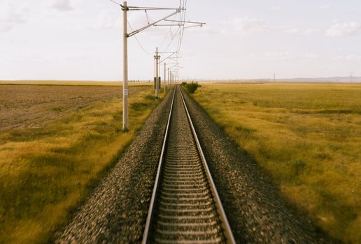 A long railway track surrounded by vast yellow fields under a clear sky, showcasing rural scenery.